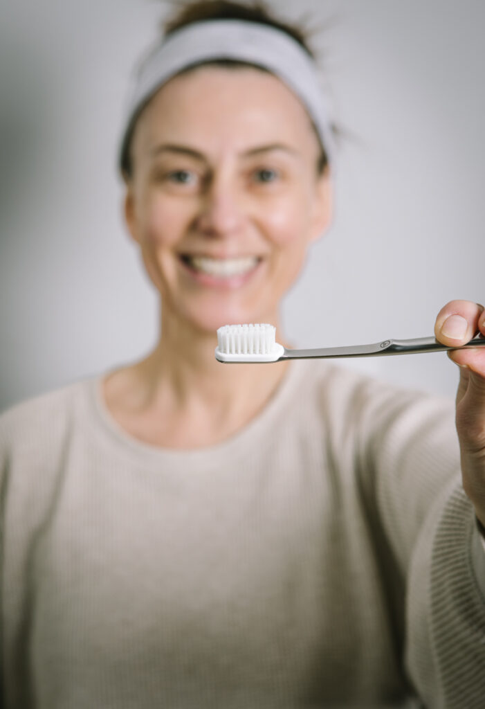 www.asimplelifetime.com Finding a Sustainable Toothbrush, Harder Than You Might Think. Closeup of the Lifetime toothbrush with a smily woman in the background.
